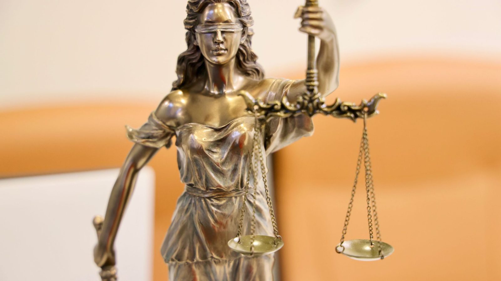 Bronzefigur der Justitia mit Waage, im Hintergrund unscharf ein Kanzleibüro